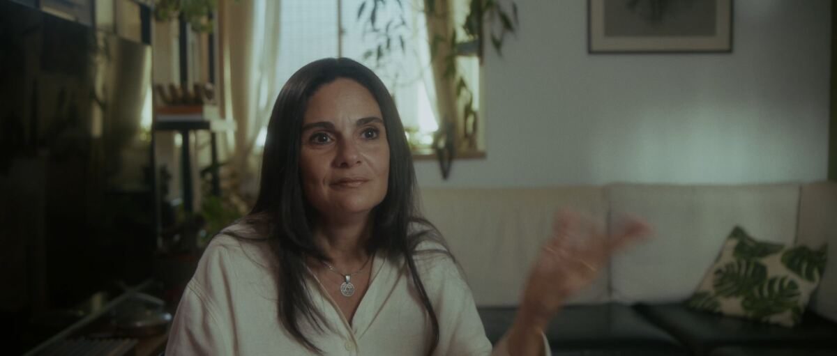 Mulher sentada na sala de casa, falando para a câmera, em cena do documentário Um Shabat na Outra Margem do Rio